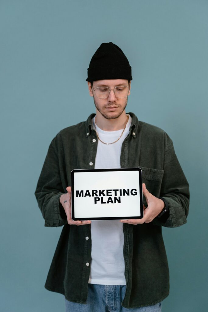 pexels-photo-7550307-7550307 Adult wearing casual clothing holding a tablet that reads 'Marketing Plan'.